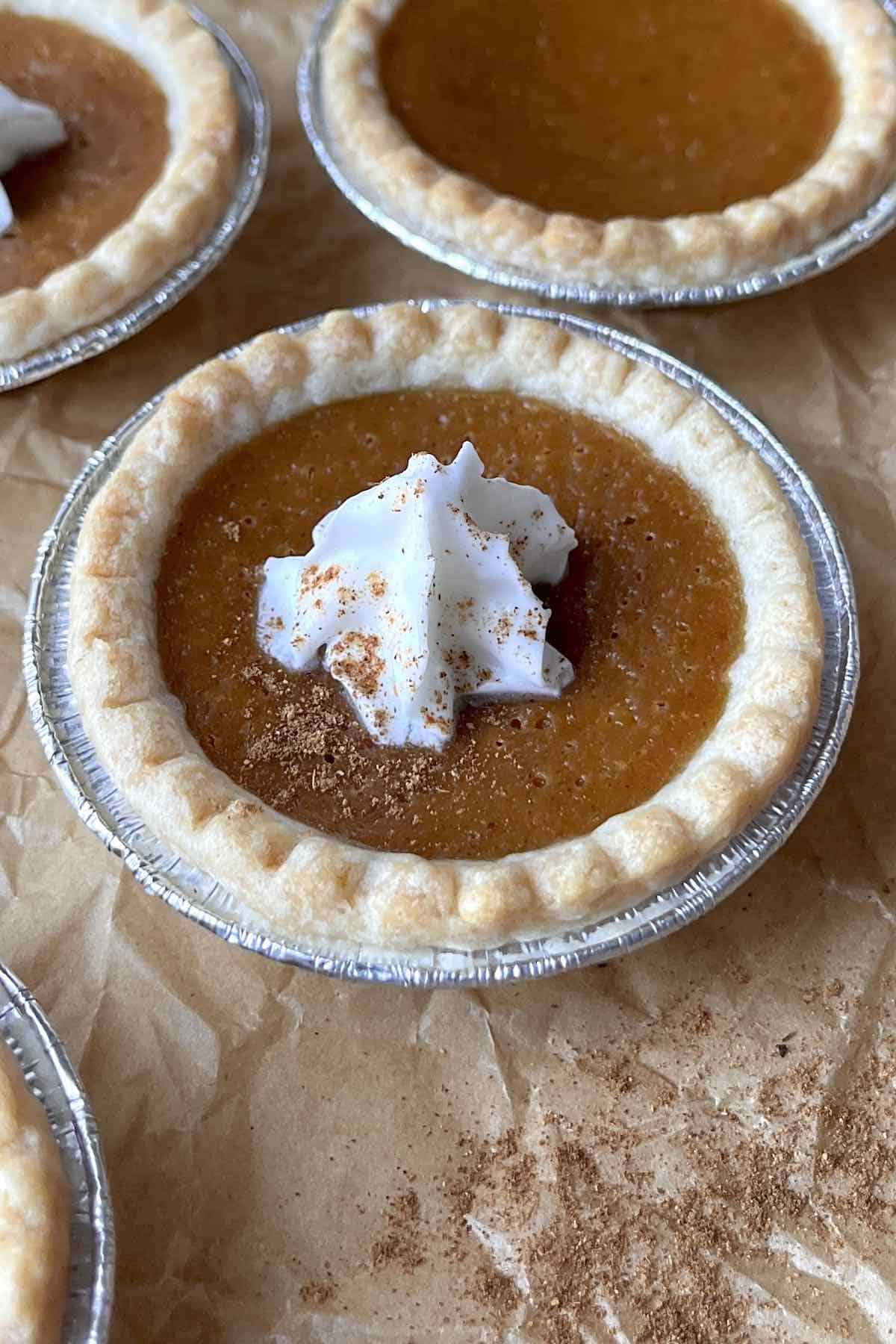 Mini pumpkin pie tart topped with whipped cream on a piece of brown parchment paper.