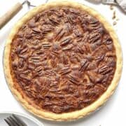 Condensed milk pecan pie with a pie server and stack of plates and forks beside it.