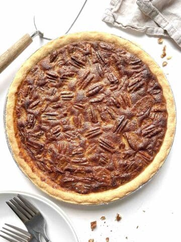 Condensed milk pecan pie with a pie server and stack of plates and forks beside it.