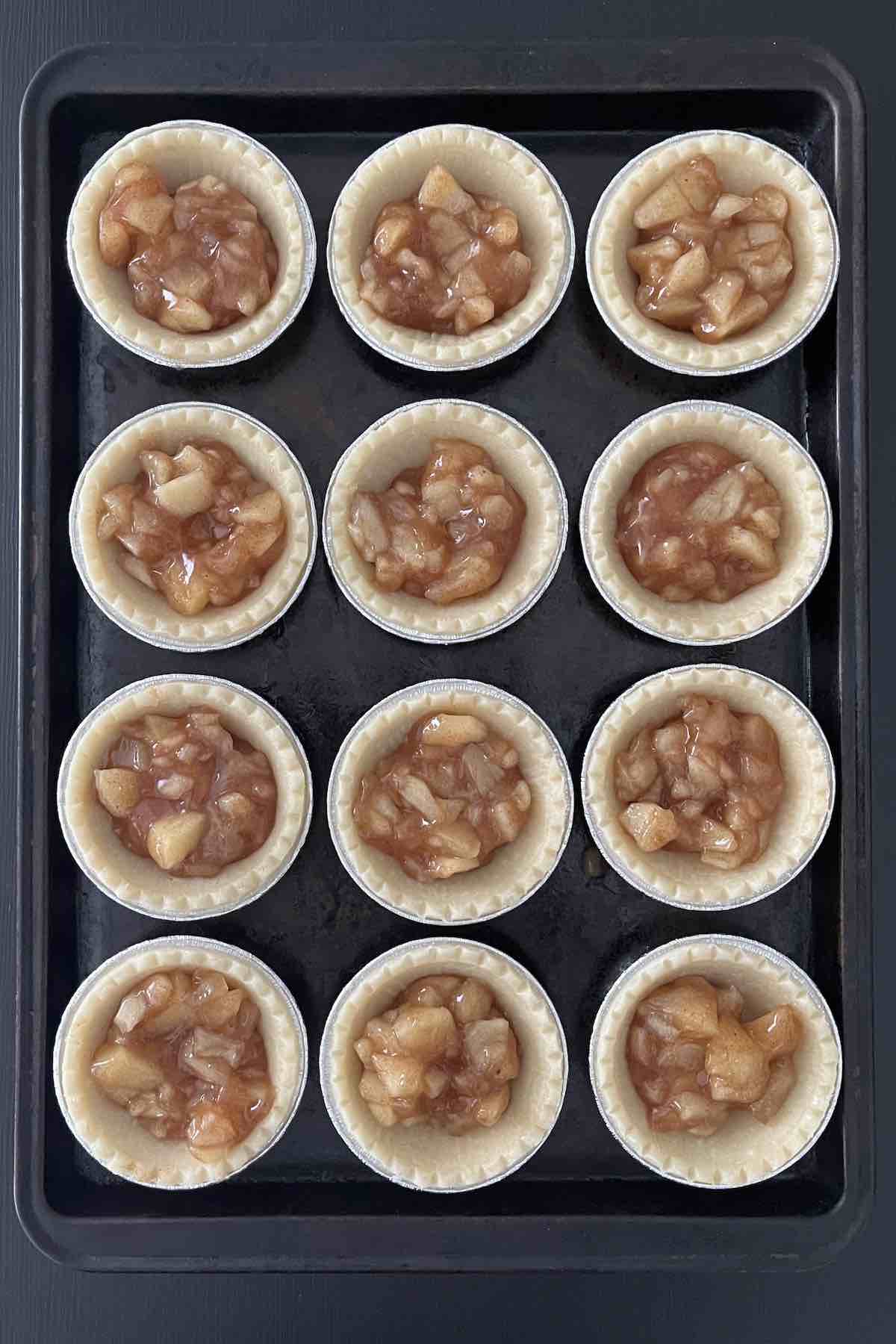 Frozen tart shells filled with the apple pie filling on a baking sheet.