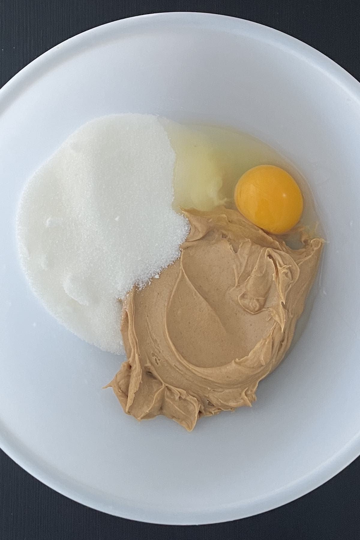 Peanut butter, sugar, and egg in a bowl.