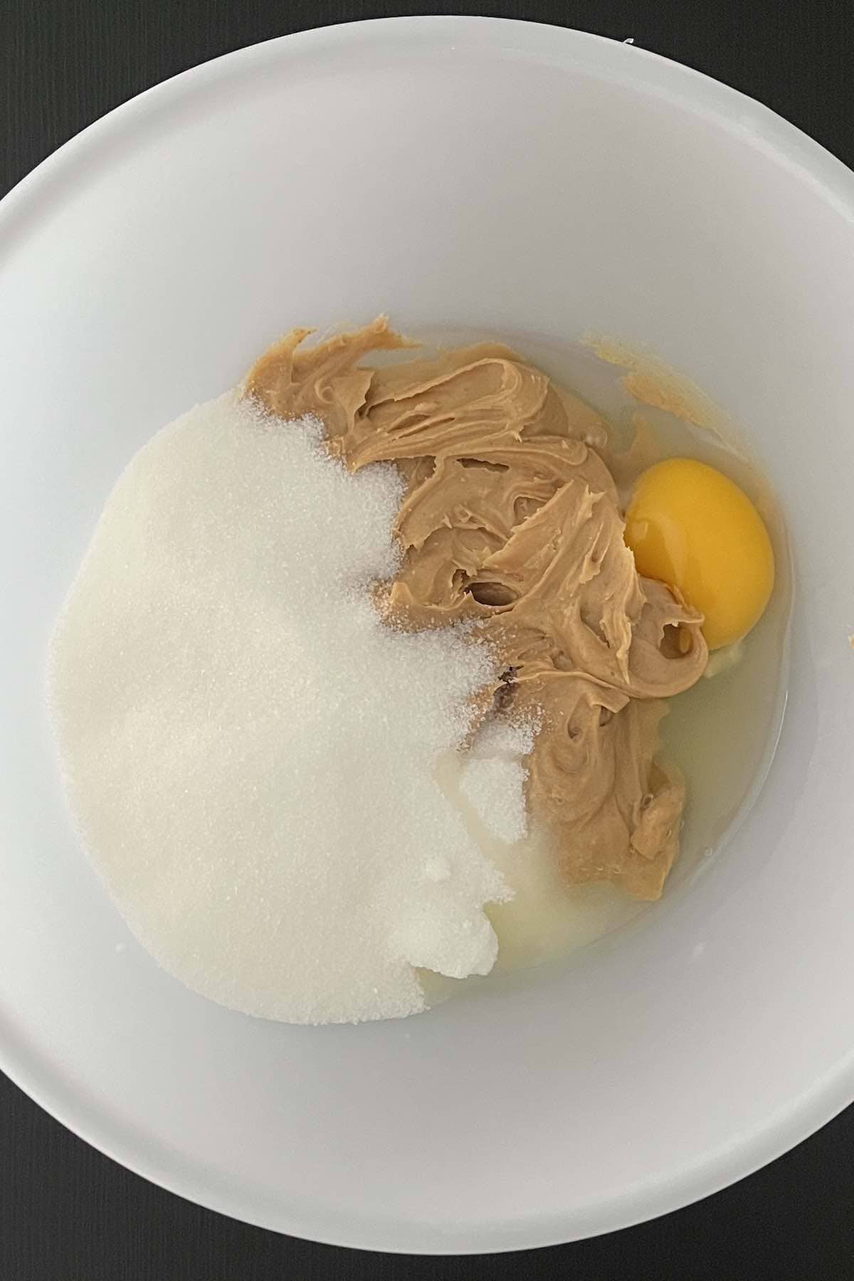 Peanut butter, sugar, and an egg in a bowl.