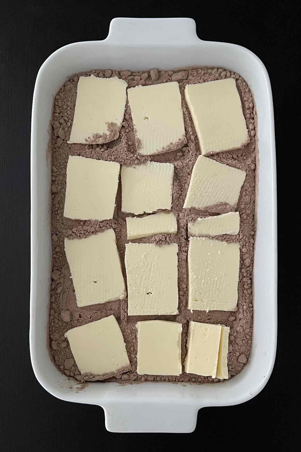 Cherry pie filling in baking dish topped with chocolate cake mix and butter slices.