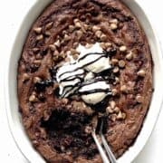 Chocolate pudding dump cake in a white baking dish topped with vanilla ice cream and chocolate sauce.
