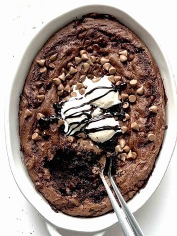 Chocolate pudding dump cake in a white baking dish topped with vanilla ice cream and chocolate sauce.