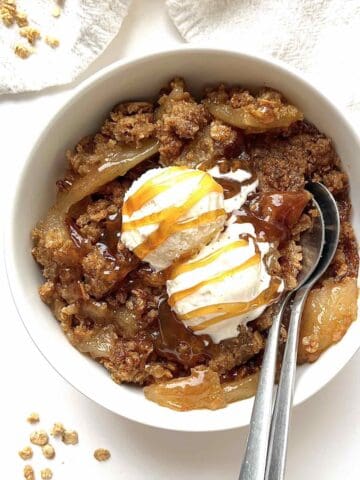 Granola apple crisp in a bowl topped with two scoops of ice cream and caramel drizzle.