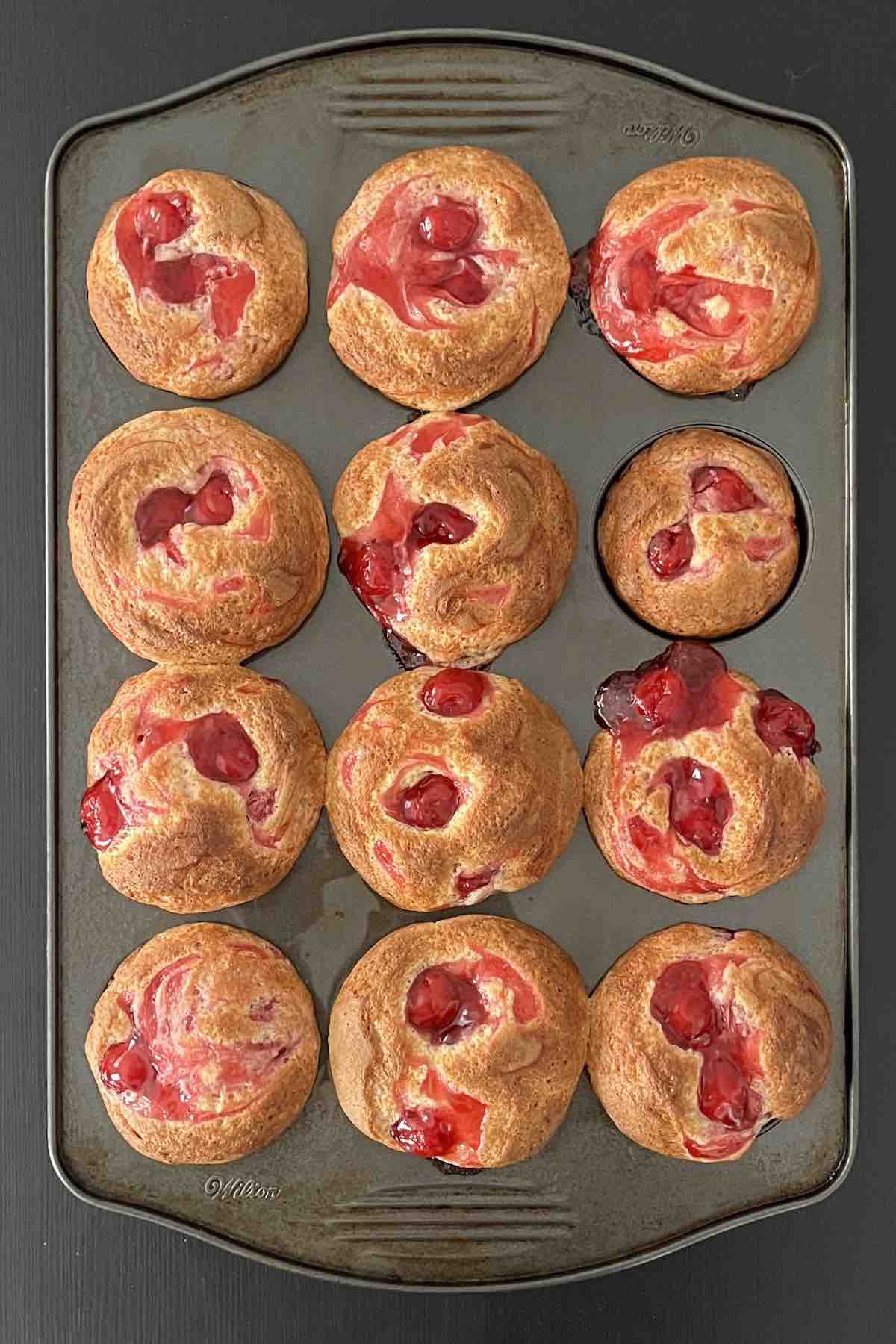 Baked cherry muffins in a muffin pan.