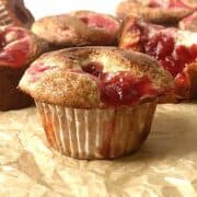 Cherry muffins with cherry pie filling on a piece of brown parchment paper.