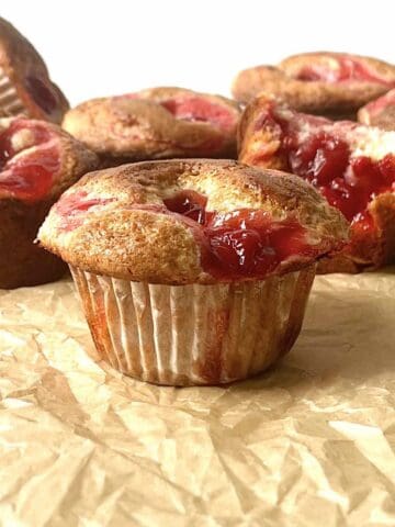 Cherry muffins with cherry pie filling on a piece of brown parchment paper.