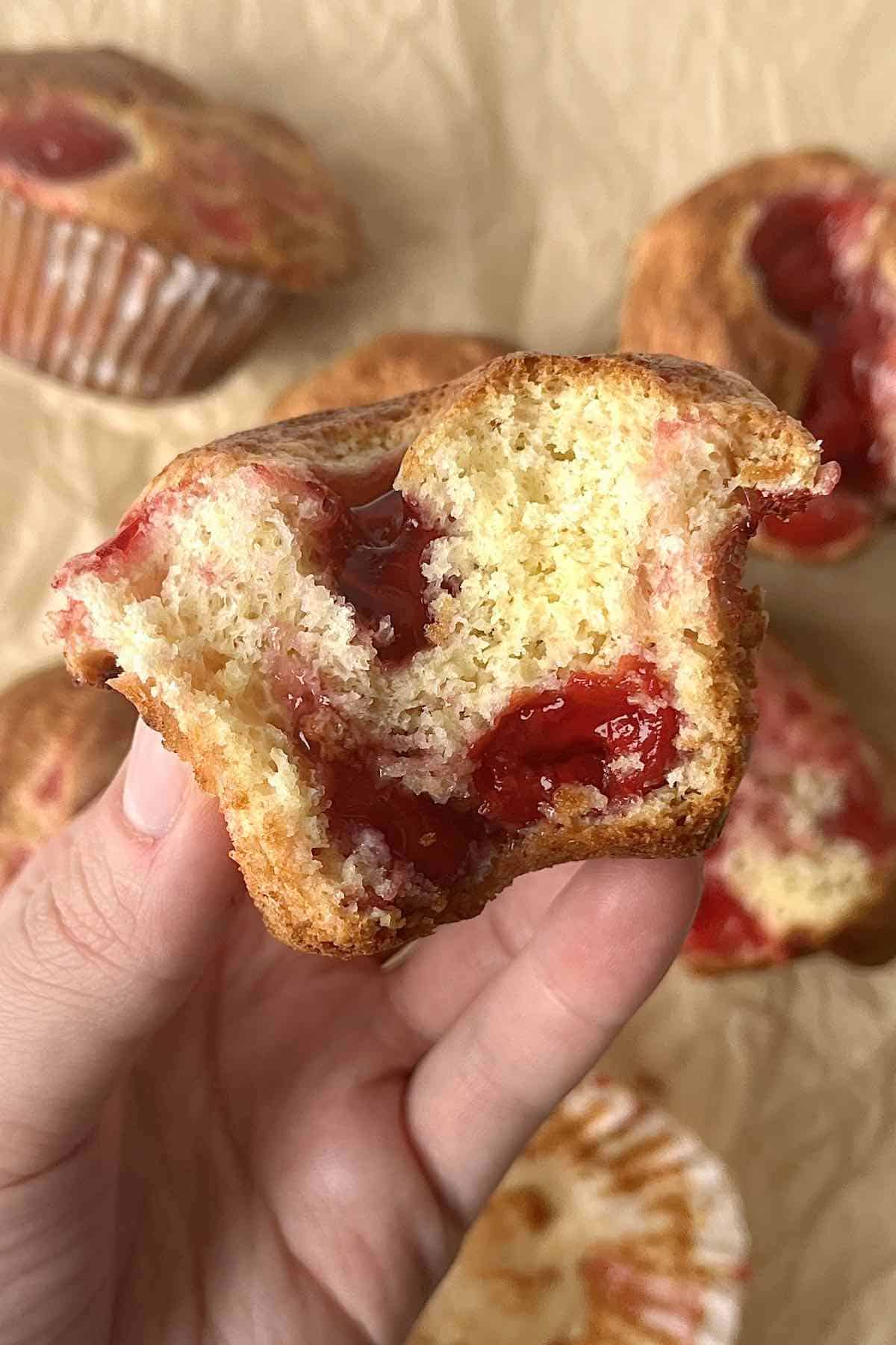 Hand holding a half eaten cherry muffin.