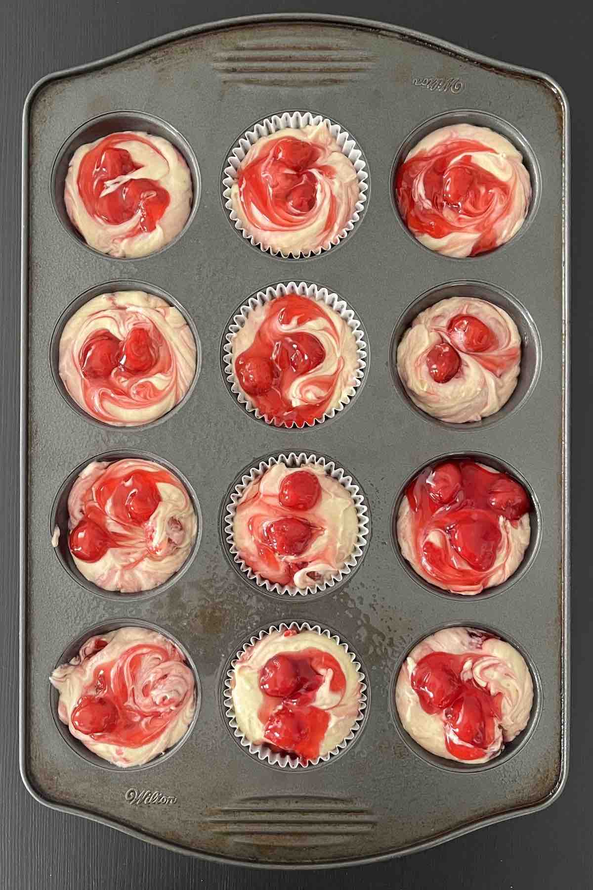 Cherry muffin batter filled in muffin liners in a muffin pan.