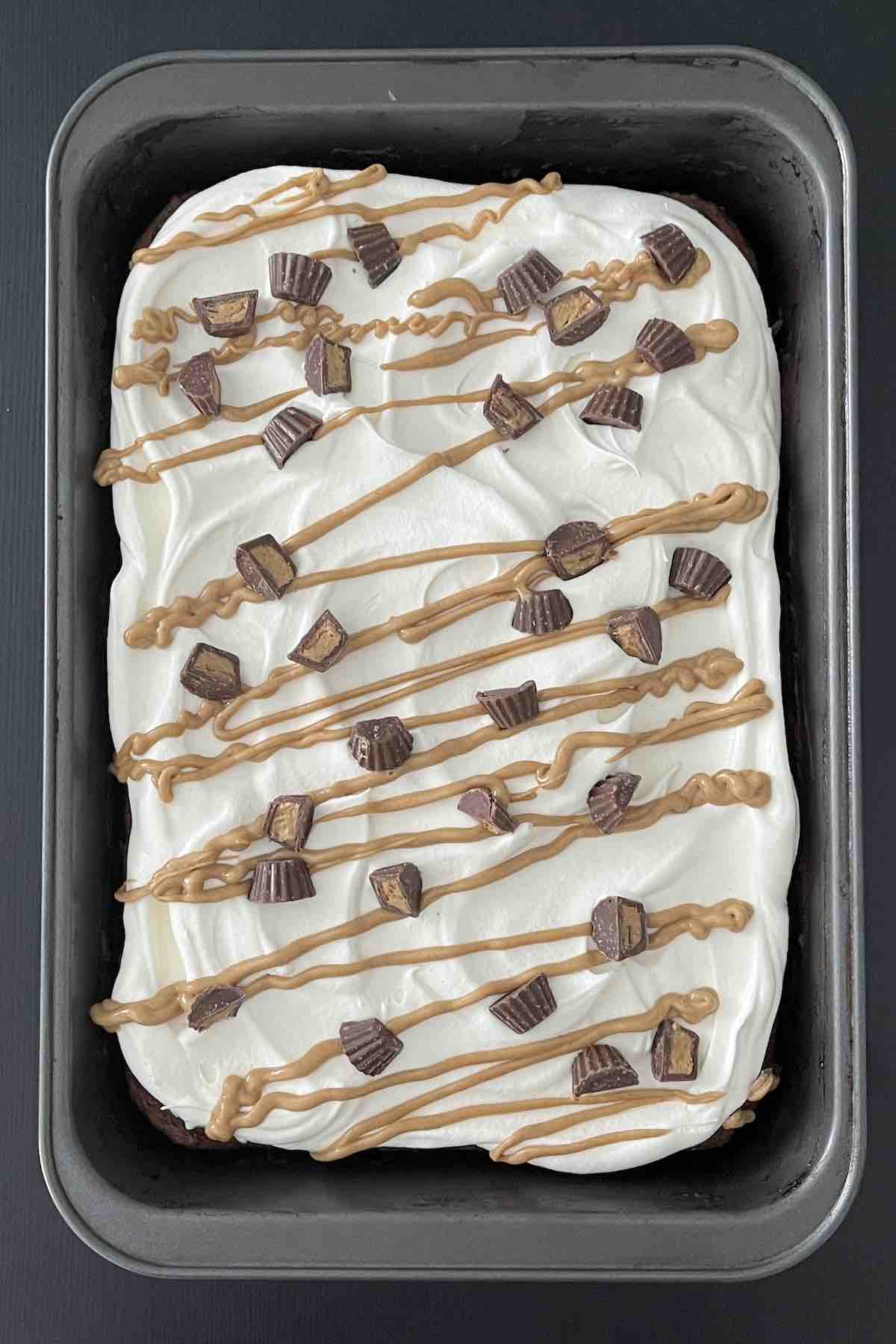 Cooled dump cake topped with whipped cream, peanut butter drizzle and peanut butter cups.