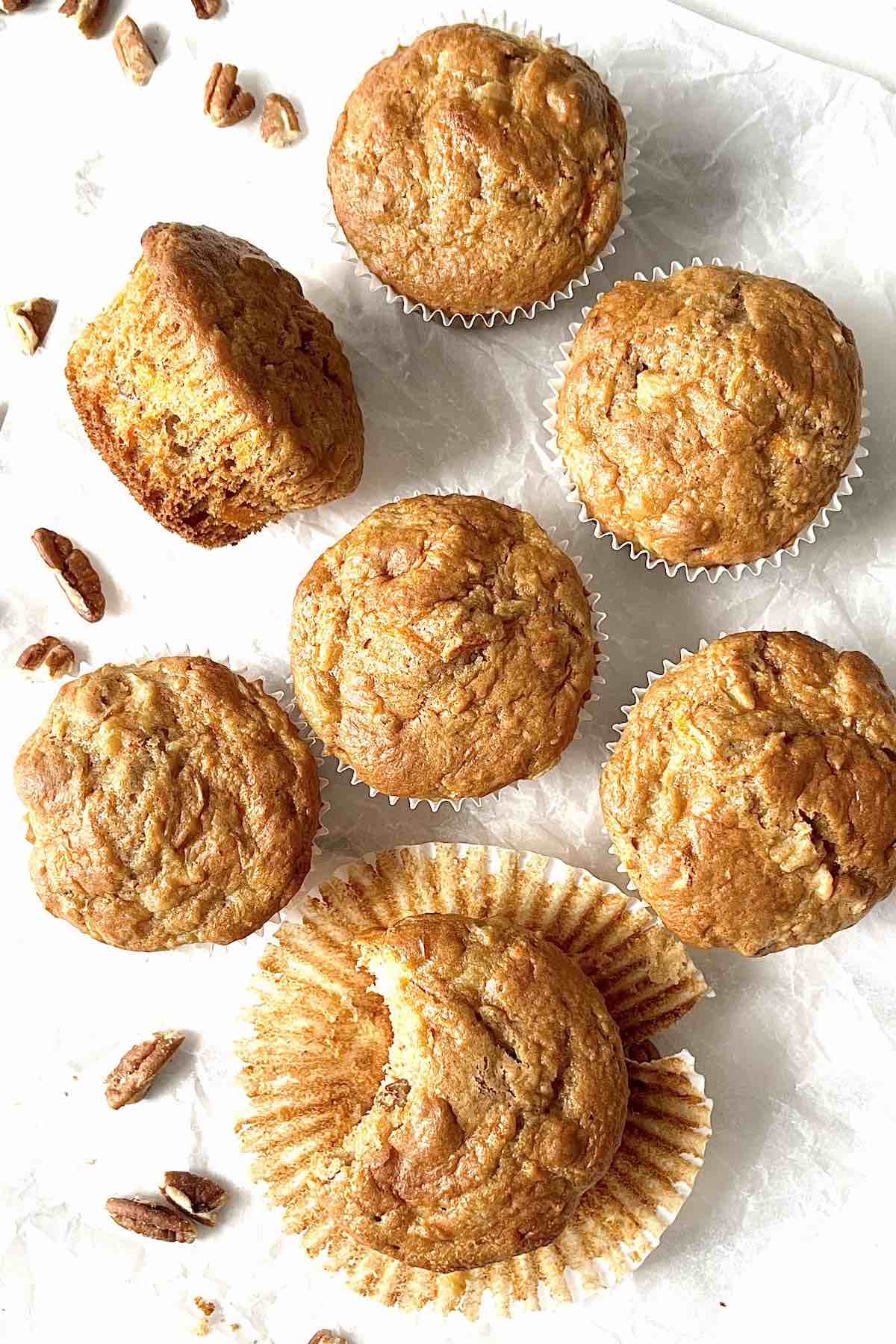 Carrot cake mix muffins and pecans scattered on a white piece of parchment paper.
