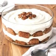 Carrot cake trifle on a wooden table with a stack of white plates and forks behind it.