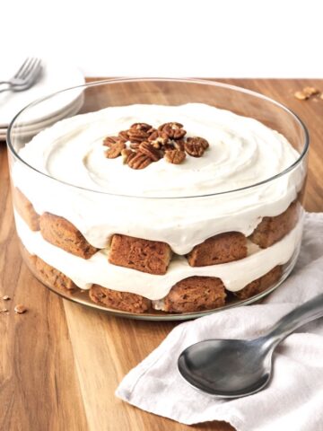 Carrot cake trifle on a wooden table with a stack of white plates and forks behind it.