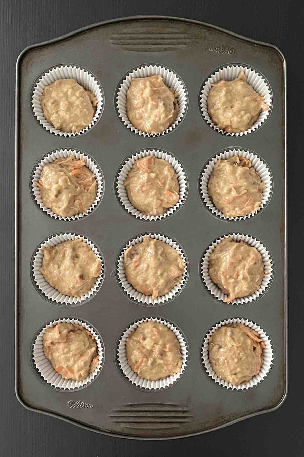 Muffin batter poured into muffin liners in a muffin pan.