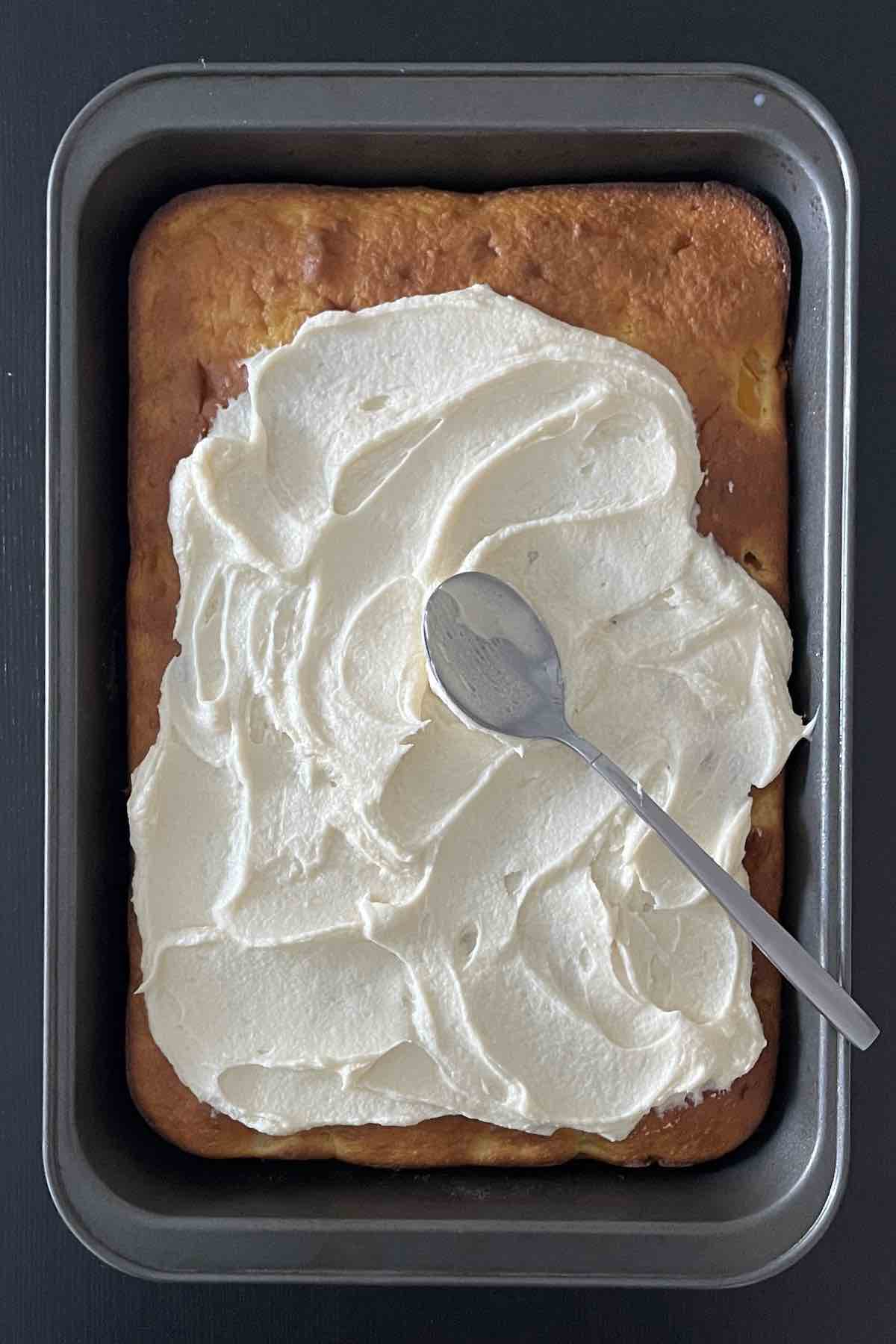 Peach cake being frosted with the back of a spoon.