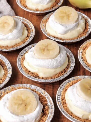 No bake mini banana cream pies scattered on a wooden table.