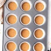 Mini graham cracker pie crusts in a muffin pan with black oven mits and a beige linen towel next to it.