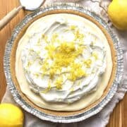 No bake lemon pie on a wooden table with a pie server and 3 lemons next to it.
