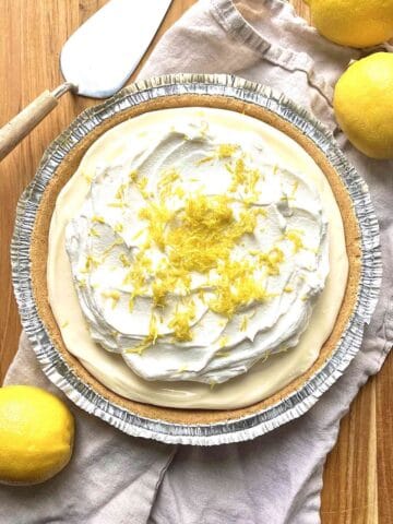 No bake lemon pie on a wooden table with a pie server and 3 lemons next to it.