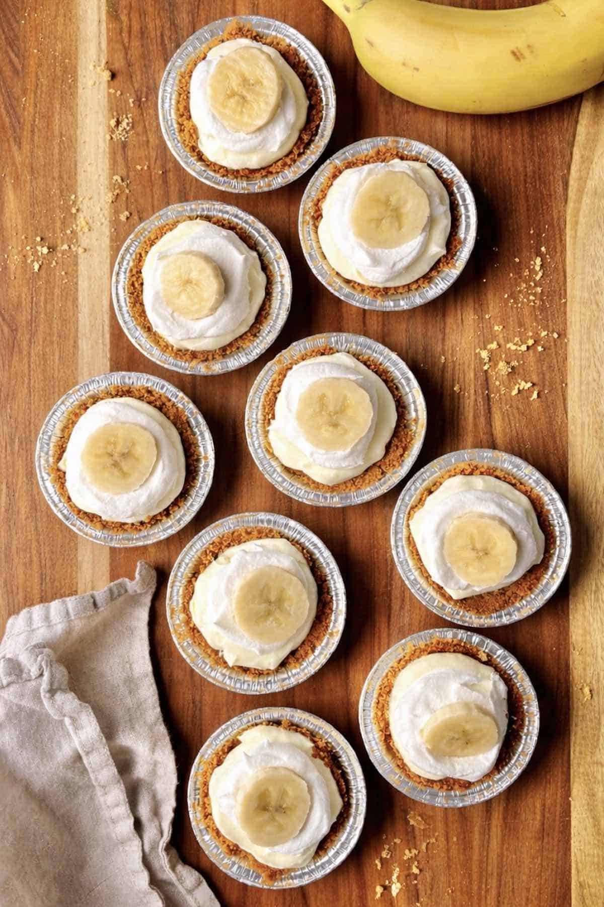 No bake mini banana cream pies scattered on a wooden table.