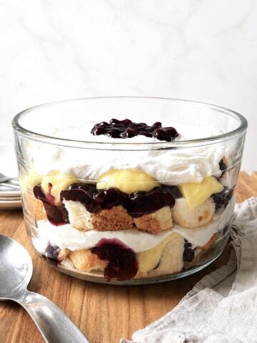 Blueberry trifle with angel food cake in a glass trifle dish on a wooden table.