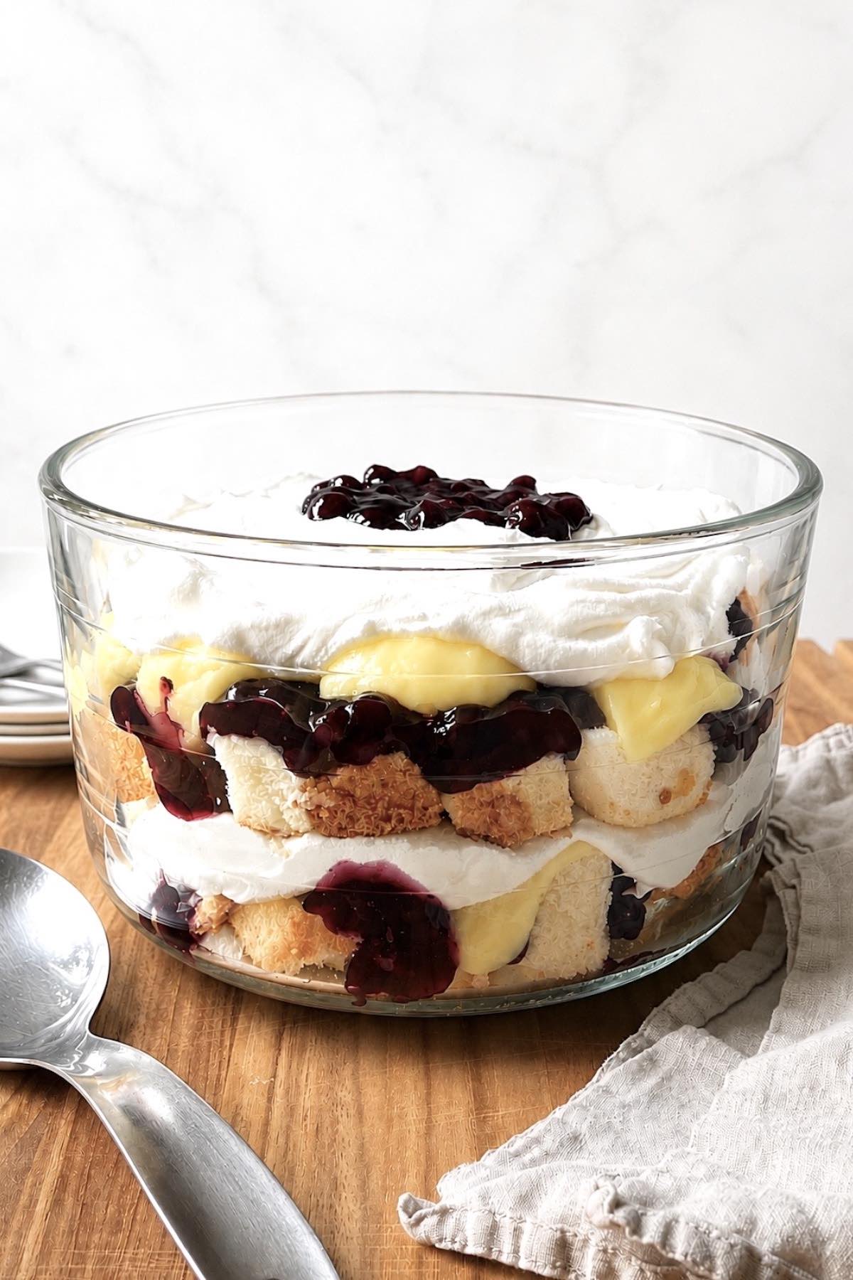 Blueberry trifle with angel food cake in a glass trifle dish on a wooden table.