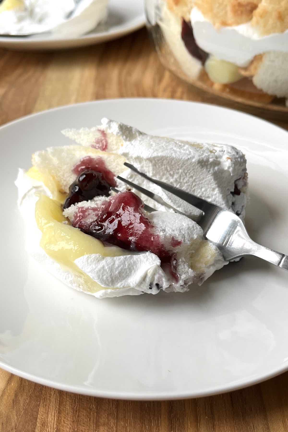 Piece of blueberry trifle on a white plate with a fork in it.