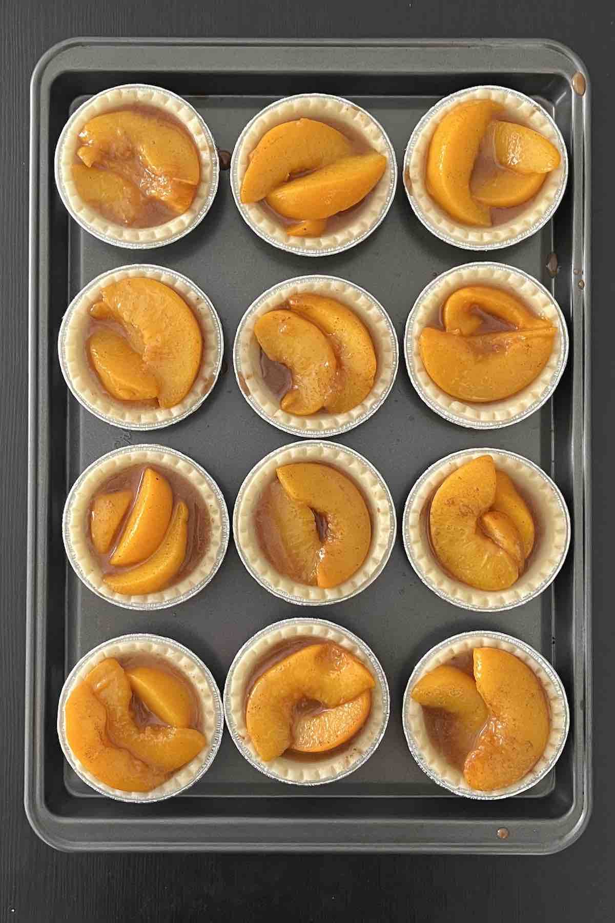 Tart shells on a baking sheet filled with peach tart filling.