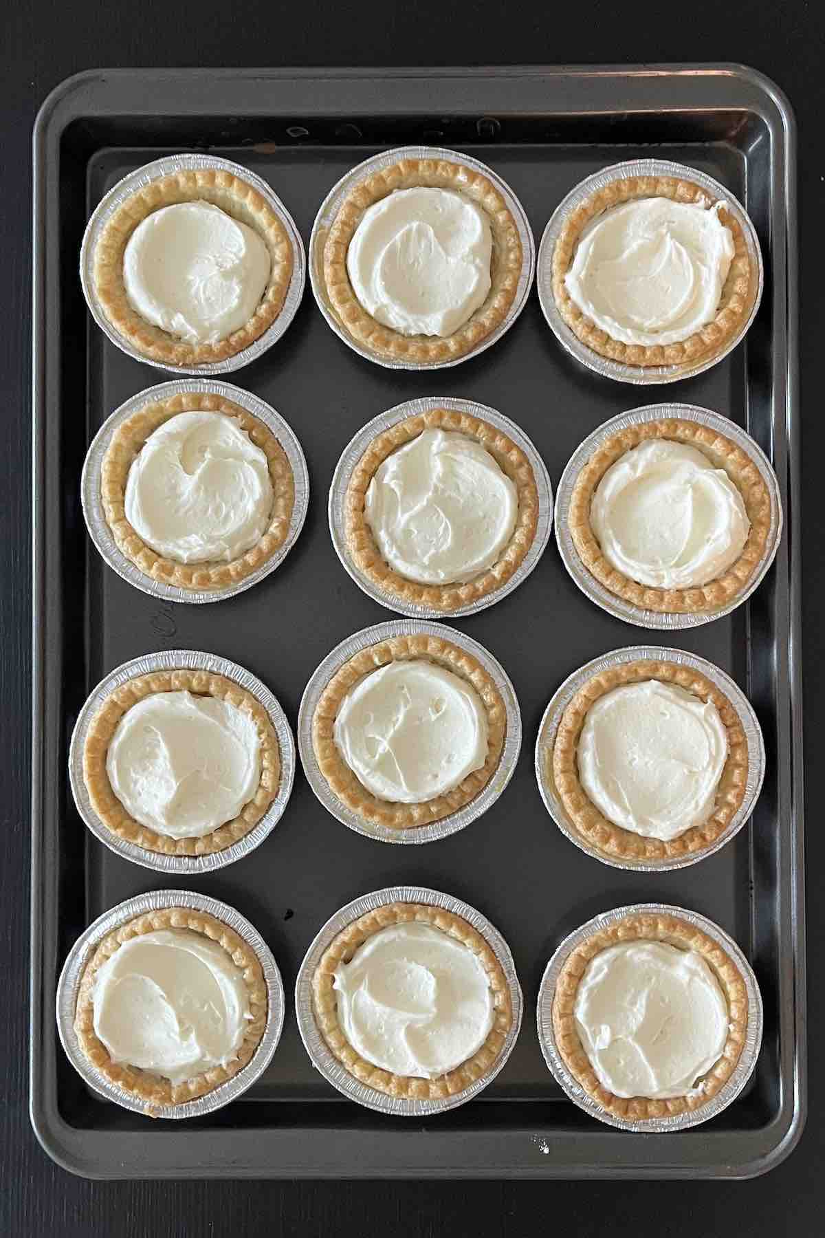 Tart shells on a baking sheet filled with pie filling.