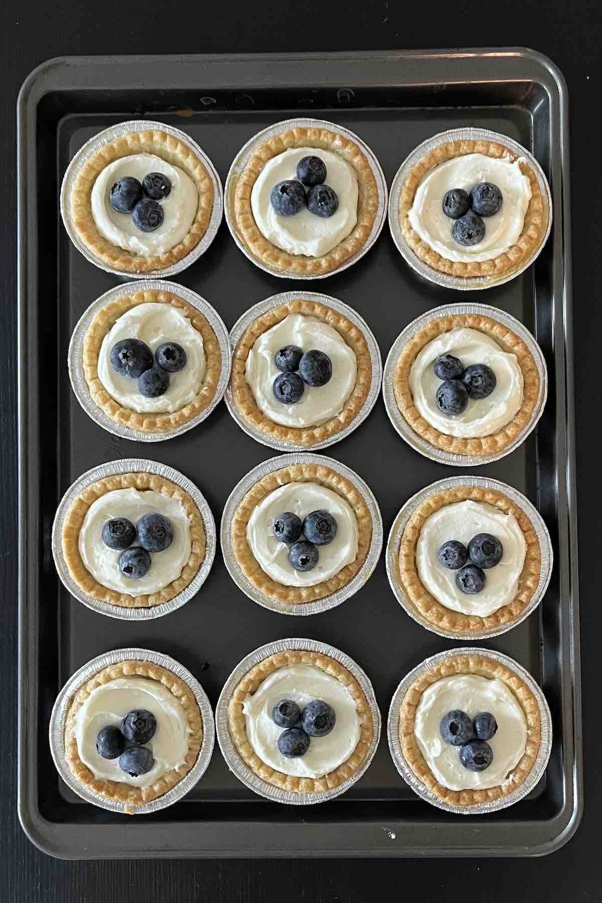 Tart shells on a baking sheet topped with fresh blueberries.