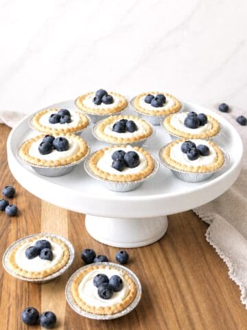 Blueberry cream cheese tarts on a white cake stand.