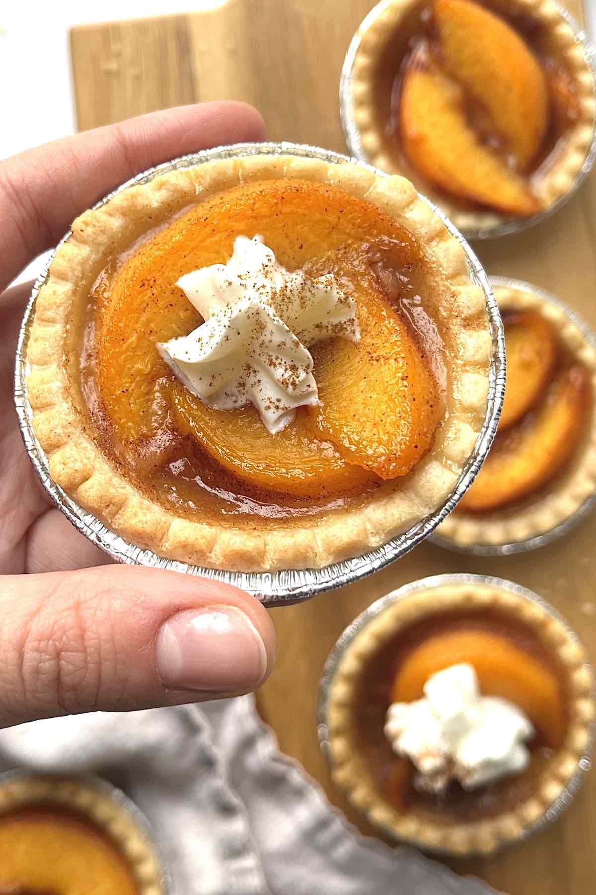 Hand holding a peach tart topped with whipped cream and cinnamon.
