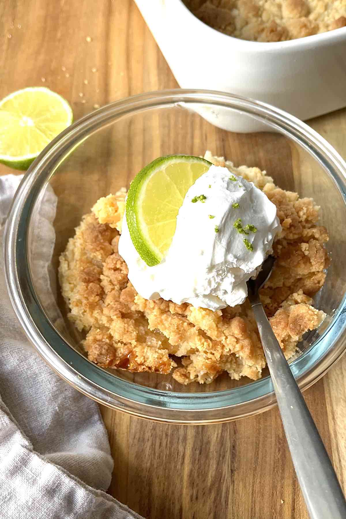 Piece of key lime dump cake in a bowl topped with cool whip and a lime wedge.