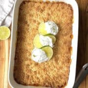 Key lime dump cake in a white baking dish topped with cool whip and lime twists.