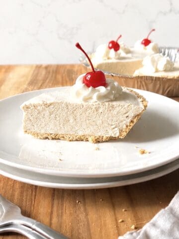 Slice of root beer float pie topped with whipped cream and a cherry on a white plate.