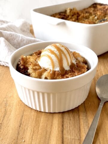 Scoop of banana dump cake in a bowl topped with vanilla ice cream and caramel sauce.