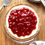 Cherry cream cheese pie on a wooden table with a stack of white plates beside it.