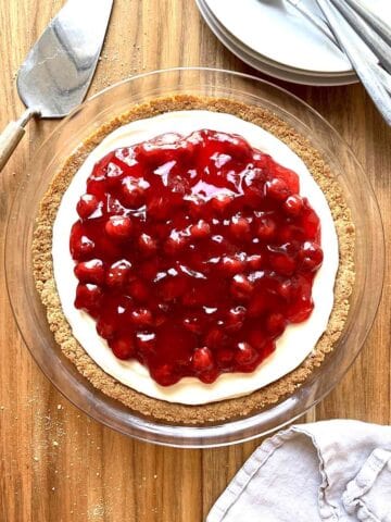 Cherry cream cheese pie on a wooden table with a stack of white plates beside it.