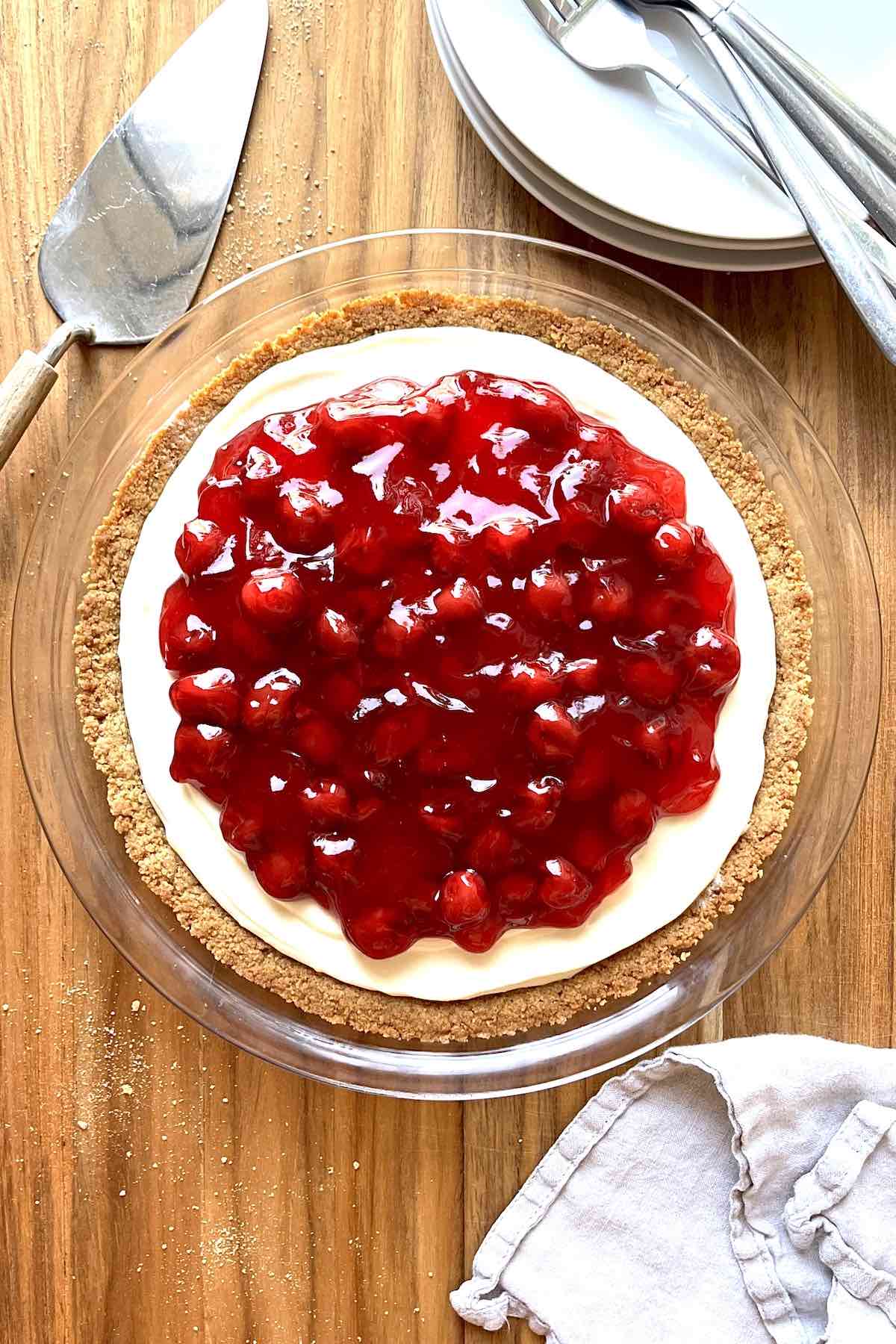 Cherry cream cheese pie on a wooden table with a stack of white plates beside it.