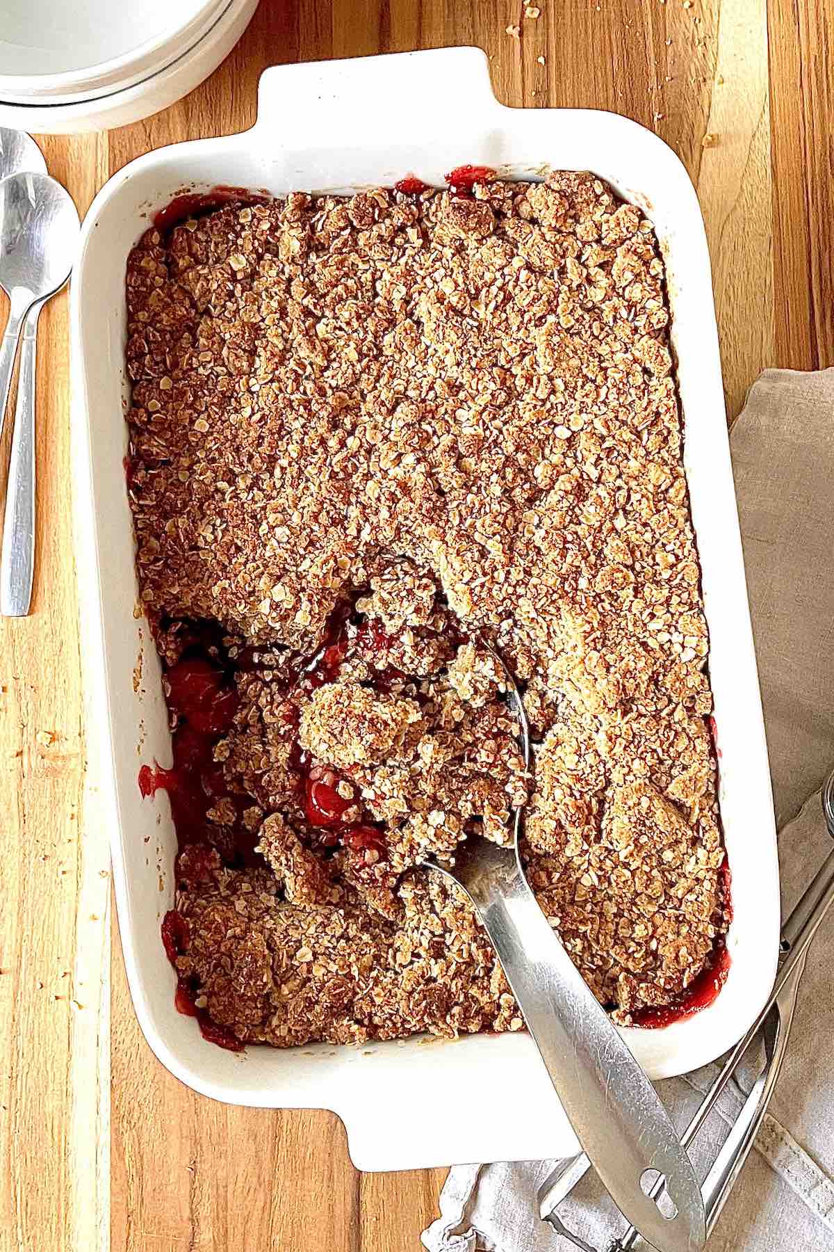 Cherry crisp in a white baking dish with a metal serving spoon in it.