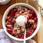 Cherry crisp in a white bowl topped with a scoop of vanilla ice cream.