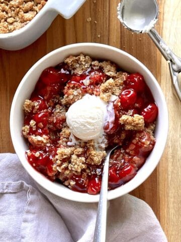 Cherry crisp in a white bowl topped with a scoop of vanilla ice cream.