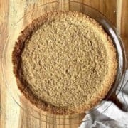 Baked graham cracker pie crust in a glass pie dish on a wooden table.