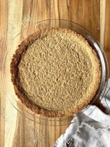Baked graham cracker pie crust in a glass pie dish on a wooden table.
