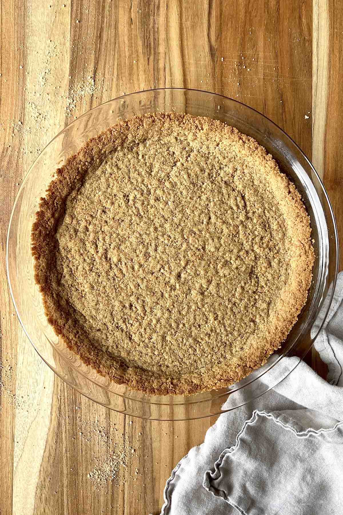 Baked graham cracker pie crust in a glass pie dish on a wooden table.