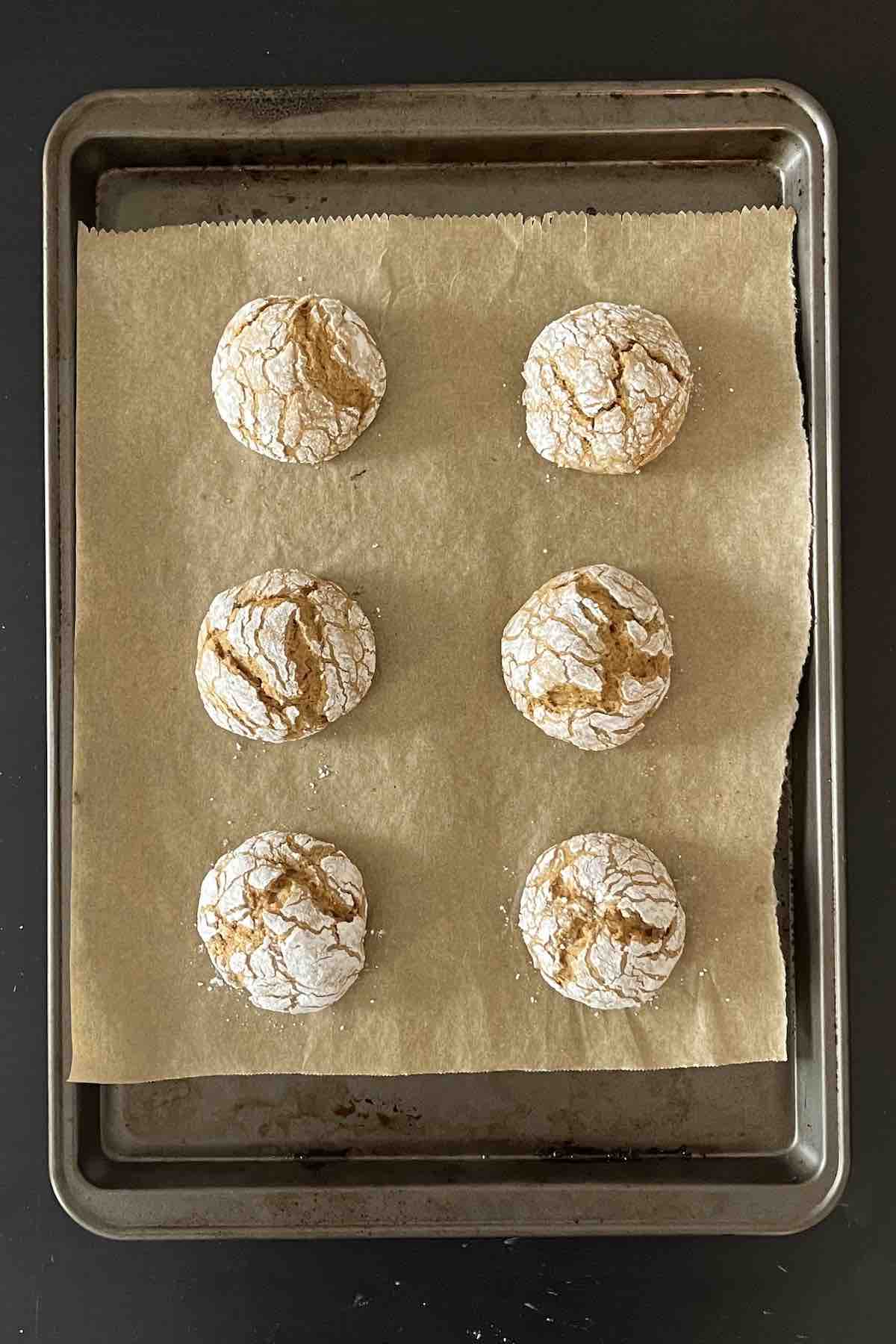 Baked pumpkin crinkle cookie dough balls lined on a baking sheet.