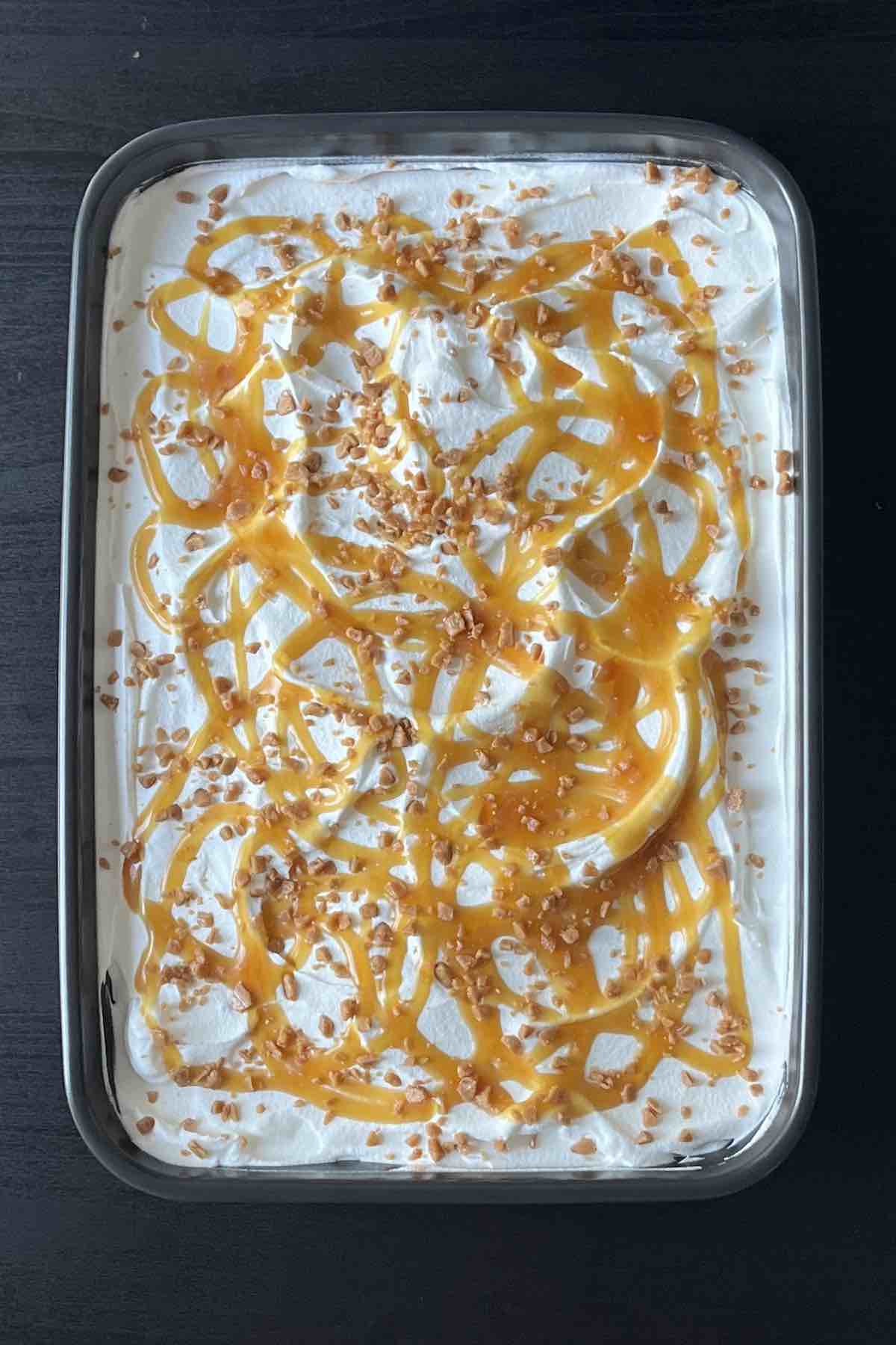 Pumpkin cake topped with a layer of cool whip, drizzled in caramel sauce and sprinkled with toffee bits.