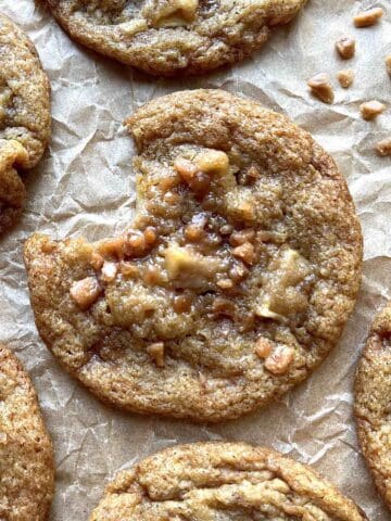 Caramel apple cookie with a bite out of it on a piece of parchment paper.